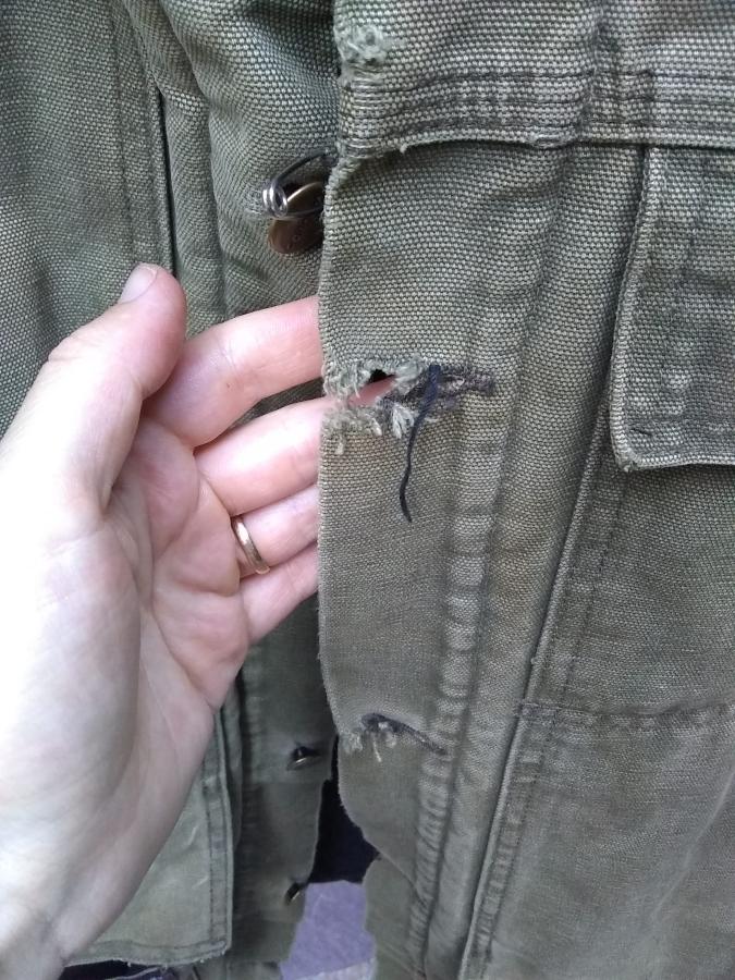 torn buttonholes on Carhart jacket, with hand shown for context