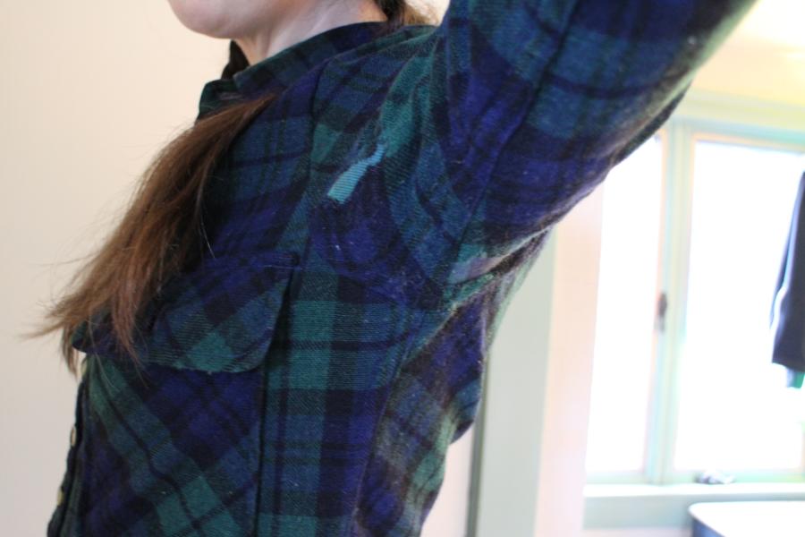 woman wearing black watch plaid shirt with armpit held up to show interior patch