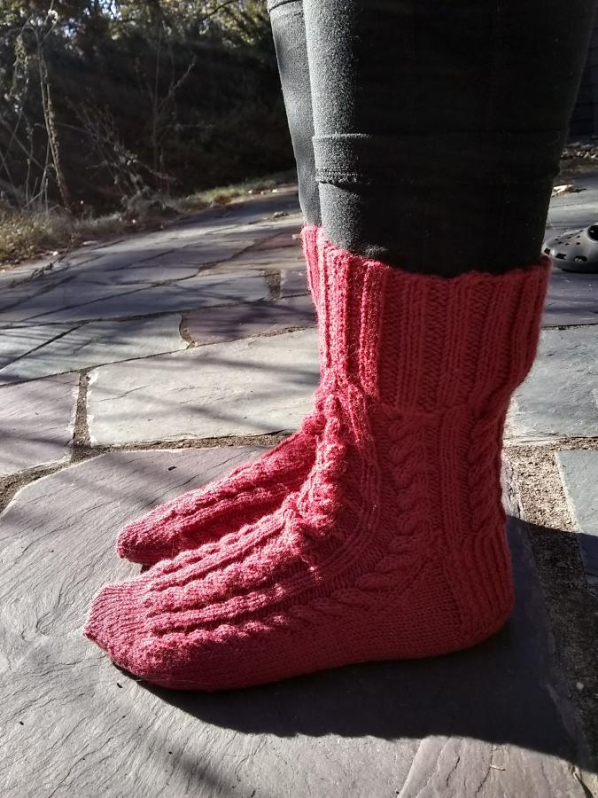 Side view of feet wearing pinkish red cabled socks outdoors on patio