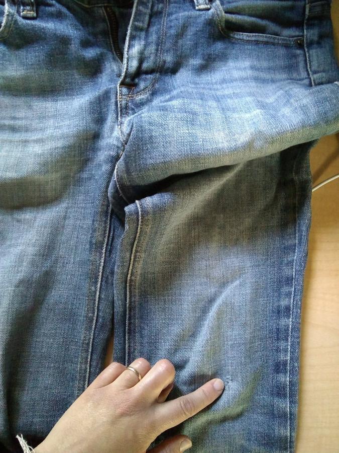 hand pointing to small hole on right knee of jeans