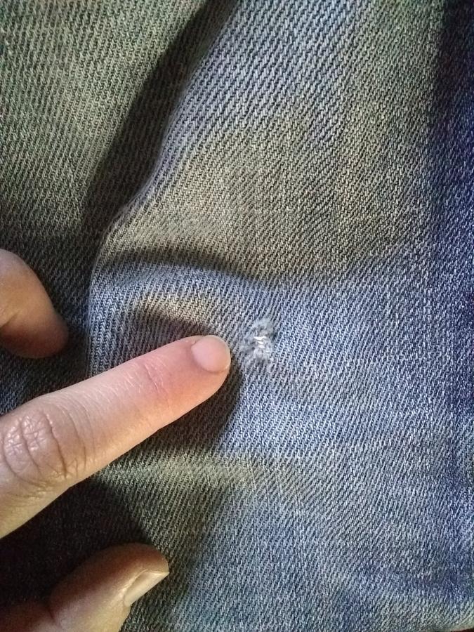 closeup of hand pointing to hole in right knee of jeans