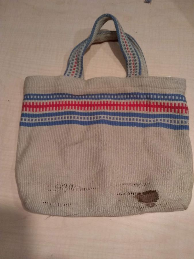 beige, blue, and red woven bag with worn fabric and stain at the bottom