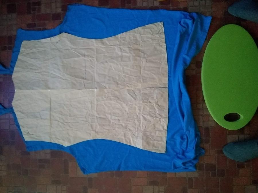 brown paper pattern of shirt back laid on top of turquoise material, with green knee pad and green-socked feet in photo