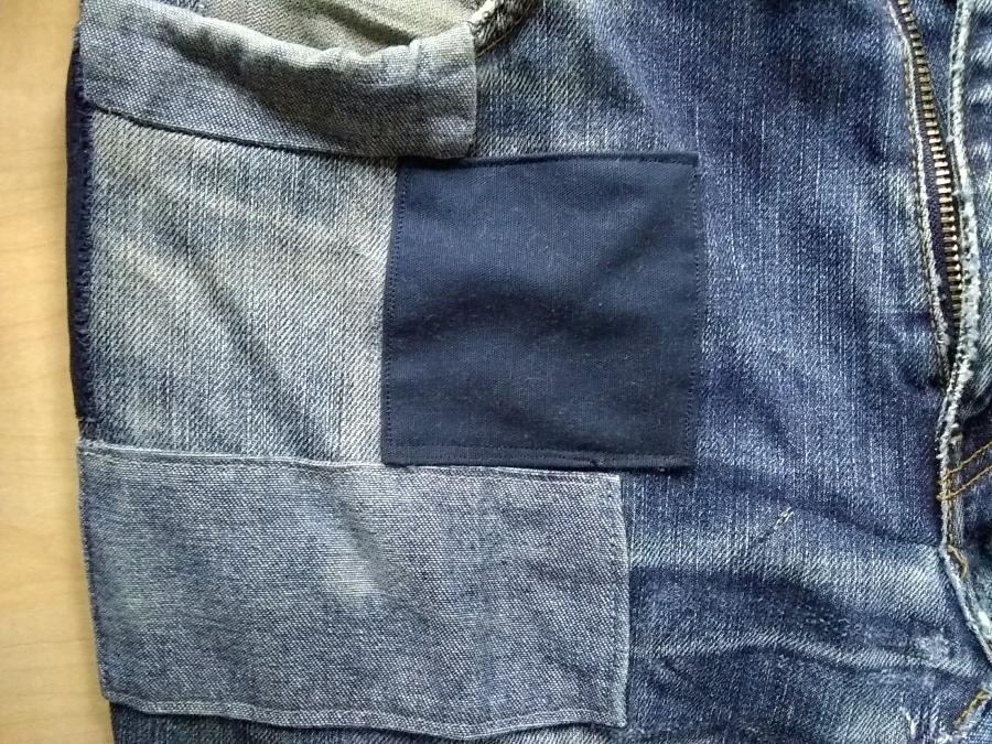 closeup of one side of jeans front under pocket, showing new (navy blue) and old (pale denim) patches