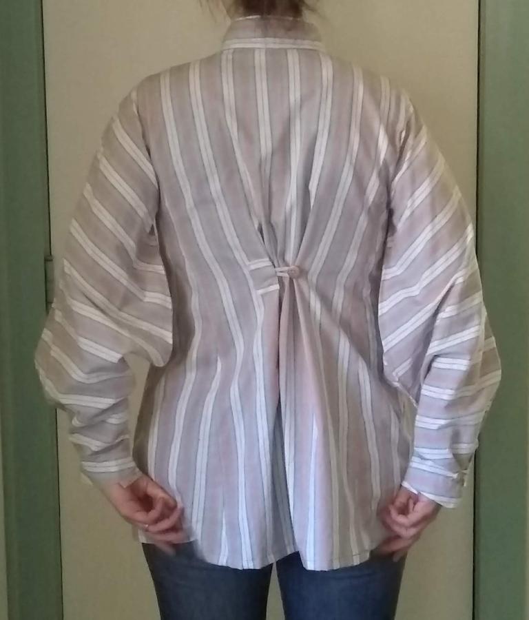 back view of woman wearing shirt with button cinching it at upper back and arms down