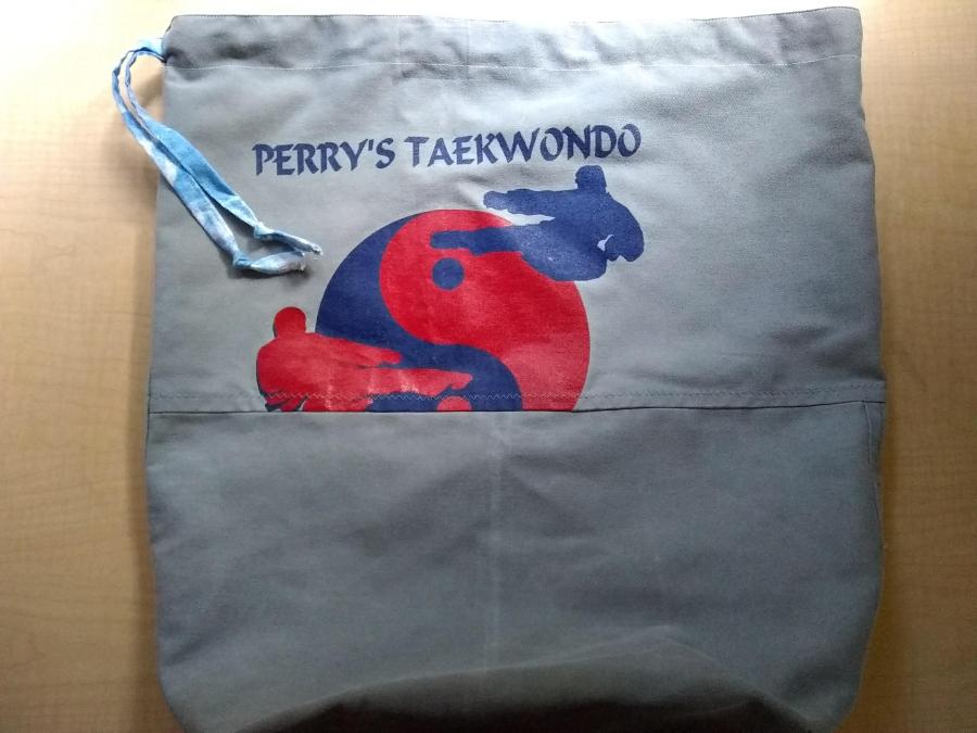 gray bag with blue cloud print drawstring and "Perry's Taekwondo" screen printing and graphic on the front. There is an obvious horizontal seam where two pieces of fabric were sewn together to make the bag