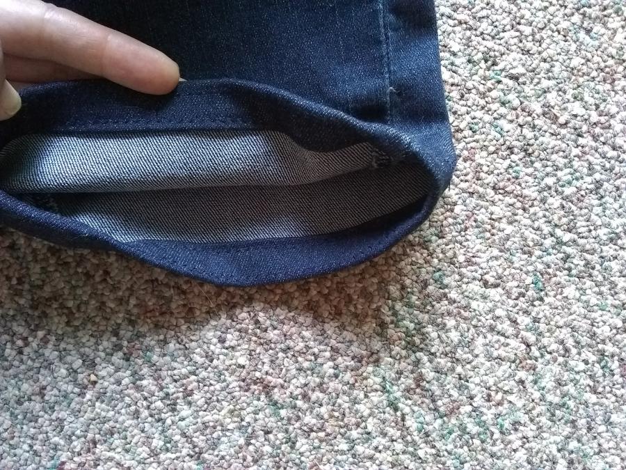 hand holding back bottom of jeans so that inside hem is visible (neat zig-zag stitches, even hem)