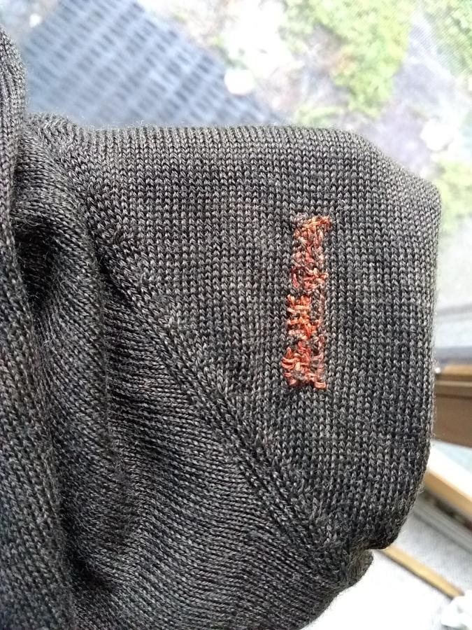 Brown sweater with visible persimmon colored rectangular mend, shown with window in background