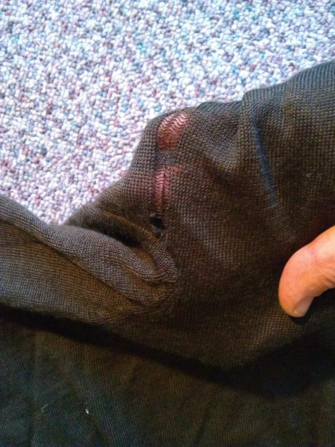 Brown knit fabric with hole in it (hand showing through loose threads)
