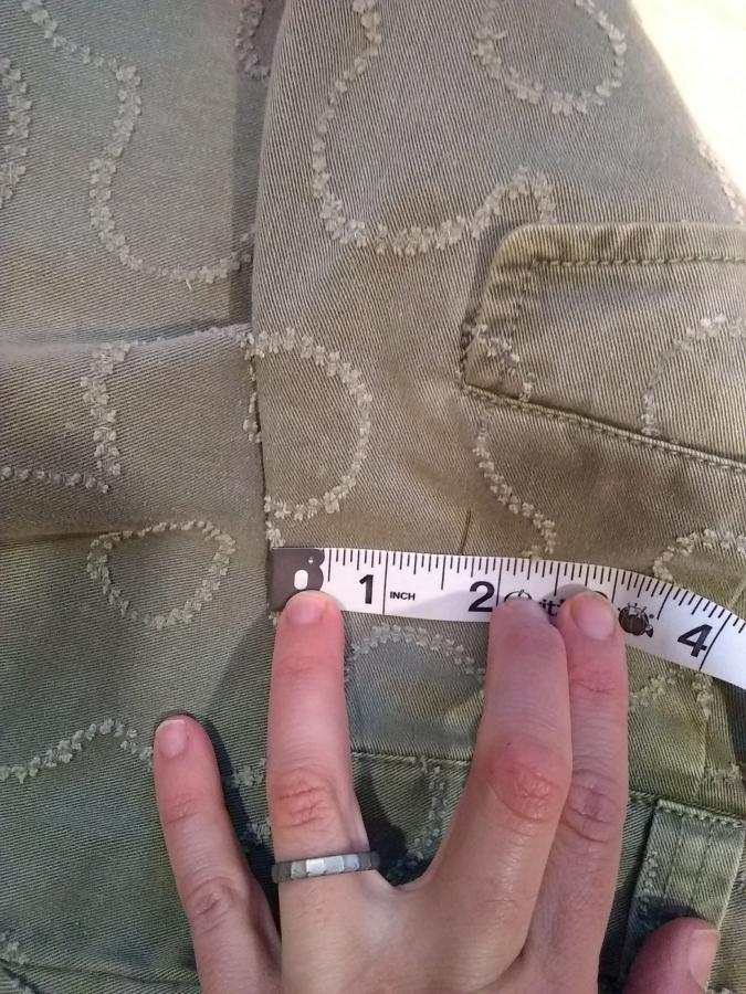 closeup of hand using measuring tape to measure part of jeans that had been cinched in with safety pin