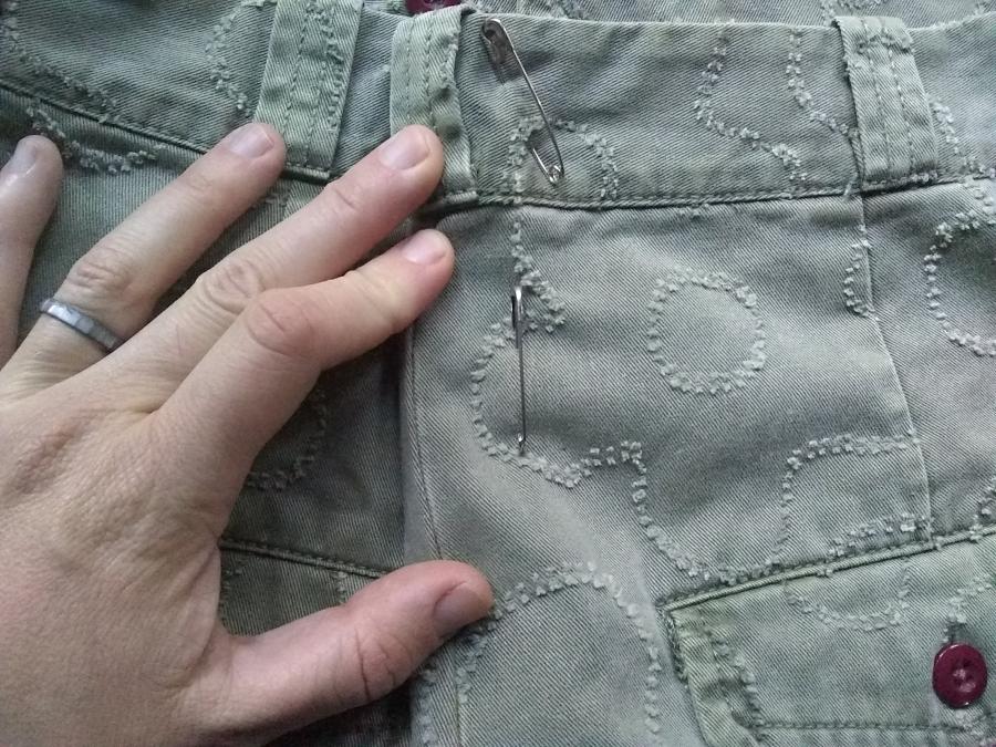 closeup of seat of green jeans and hand showing where jeans have been cinched in with safety pins at the center back waist/hip