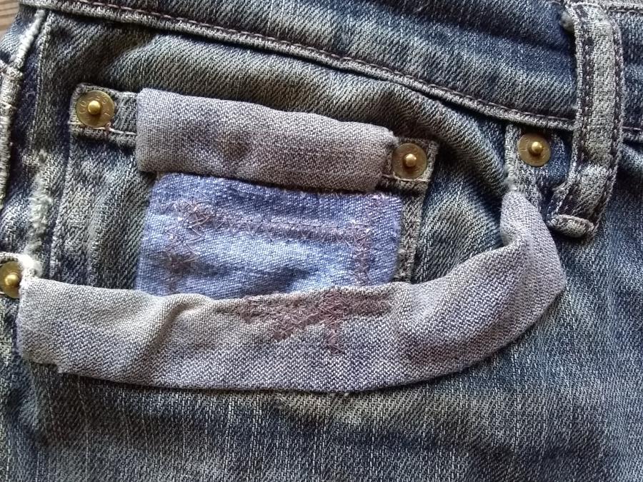 Closeup of pocket of jeans including coin pocket with multiple patches and darning