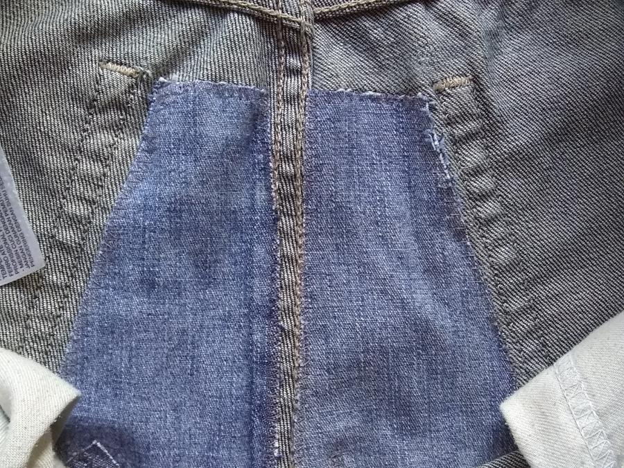 Inside view of the seat of jeans, between pockets, showing interior patches in contrasting denim applied with zig-zag stitching