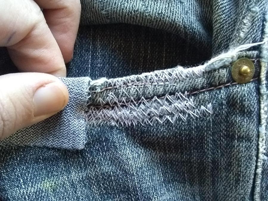 closeup of front jeans pocket and hand, showing machine darning at pocket opening