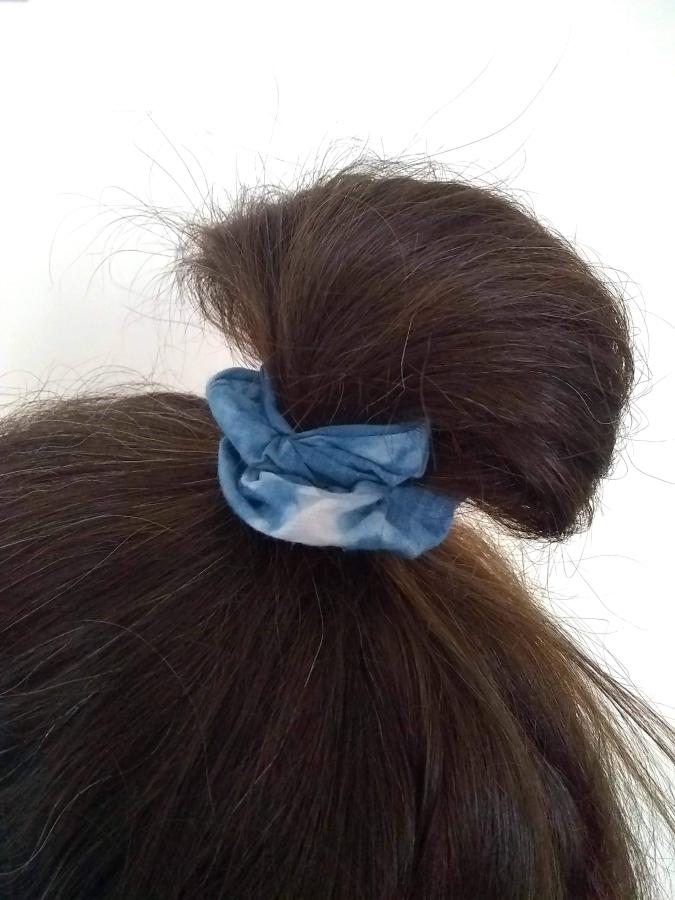 Mostly brown hair in messy bun secured by blue tie-dye scrunchie