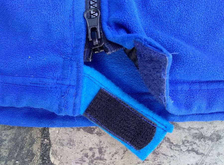 Closeup of bottom of blue fleece jacket, showing felt velcro tab at the very bottom (zipper was too short)