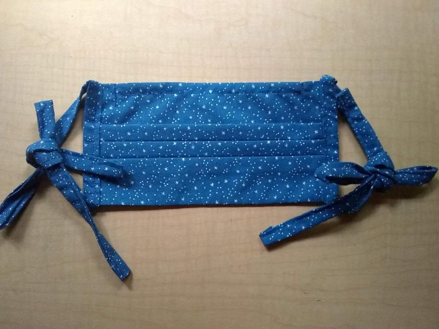 pleated facemask in blue star print with cloth ties, lying on wooden background