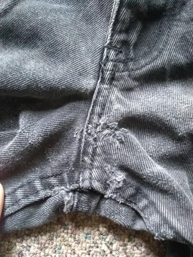 closeup of holes in crotch of black work jeans