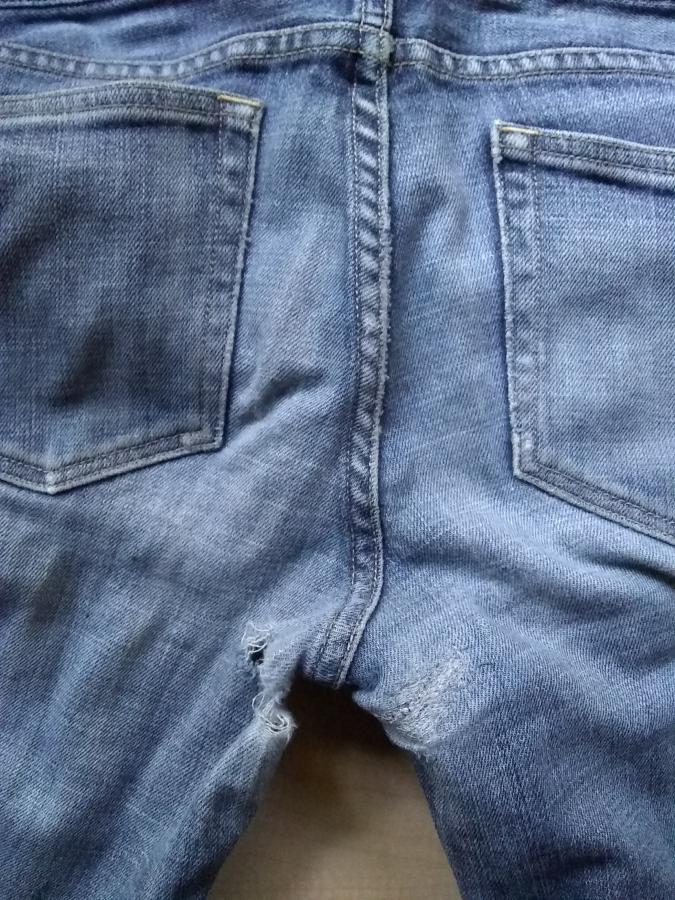 closeup of jeans backside with hole in left side and darning of previous hole in right side
