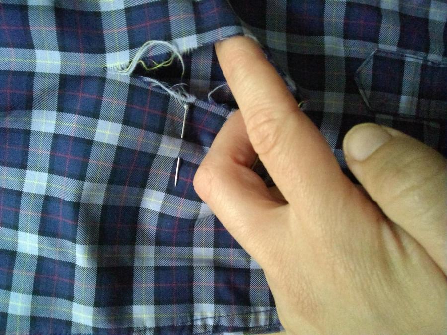 Rip in plaid shirt, closeup, with hand indicating rip