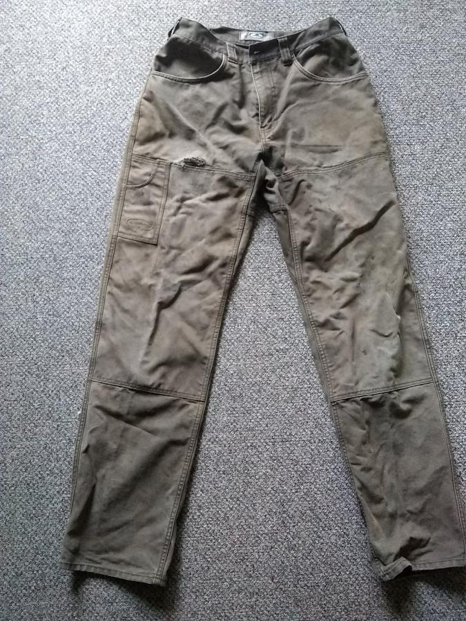 brown work pants with rip by upper thigh lying on gray rug