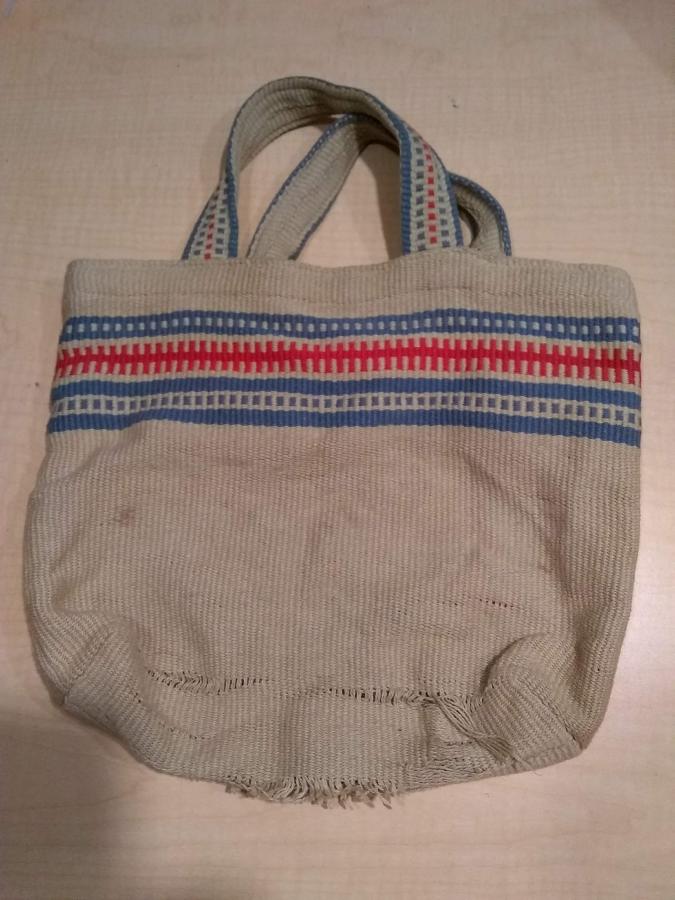 beige, blue, and red woven bag with worn fabric at the bottom
