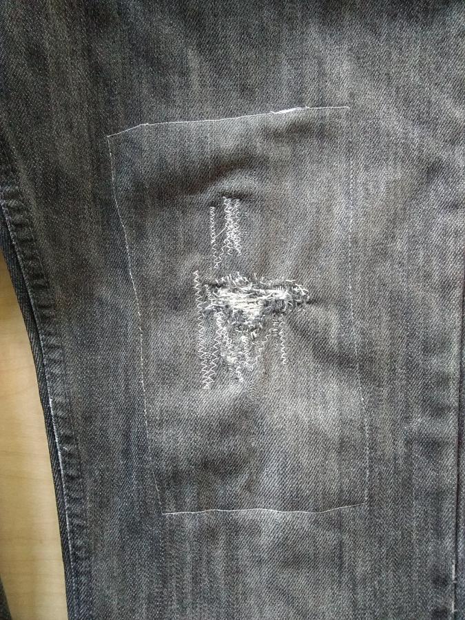 closeup of visible machine darning on knee of jeans