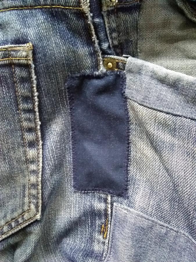 closeup of side seam of jeans, by pocket, showing new navy blue patch covering ripped seam