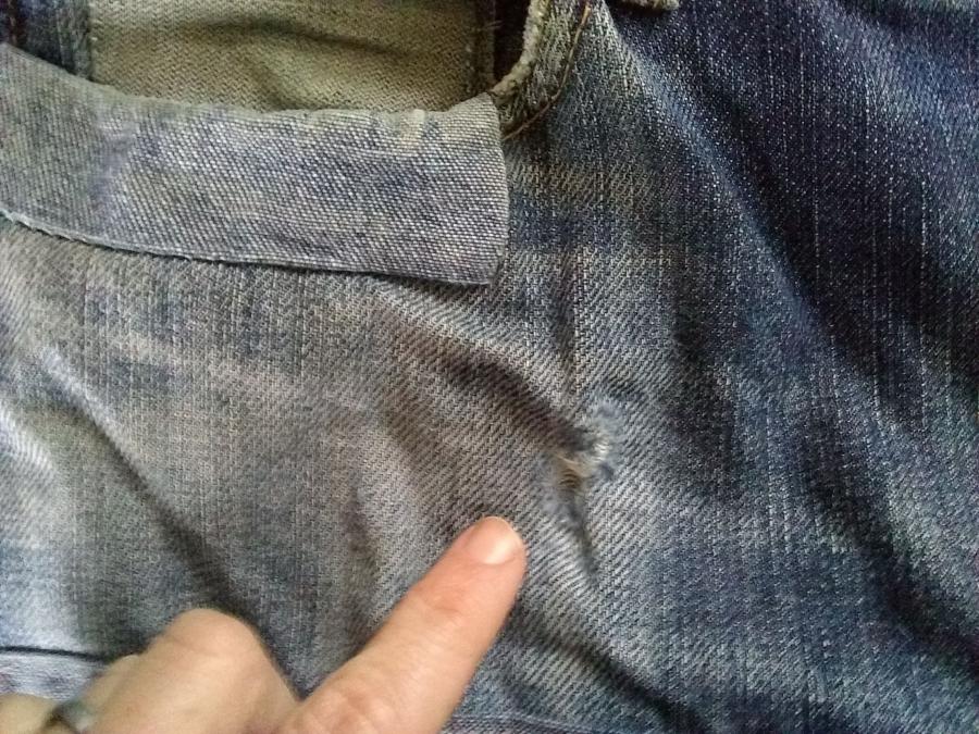 closeup view of jeans with existing patches and finger pointing to new hole under pocket
