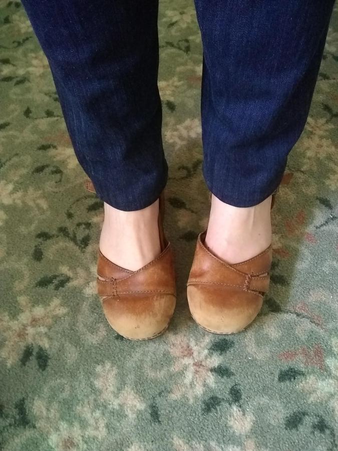 Closeup of woman's feet and ankles wearing dark jeans and brown leather clogs