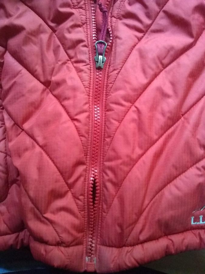 closeup of bottom of red winter jacket, showing zipper partially zipped up and with zipper teeth disengaging from eachother