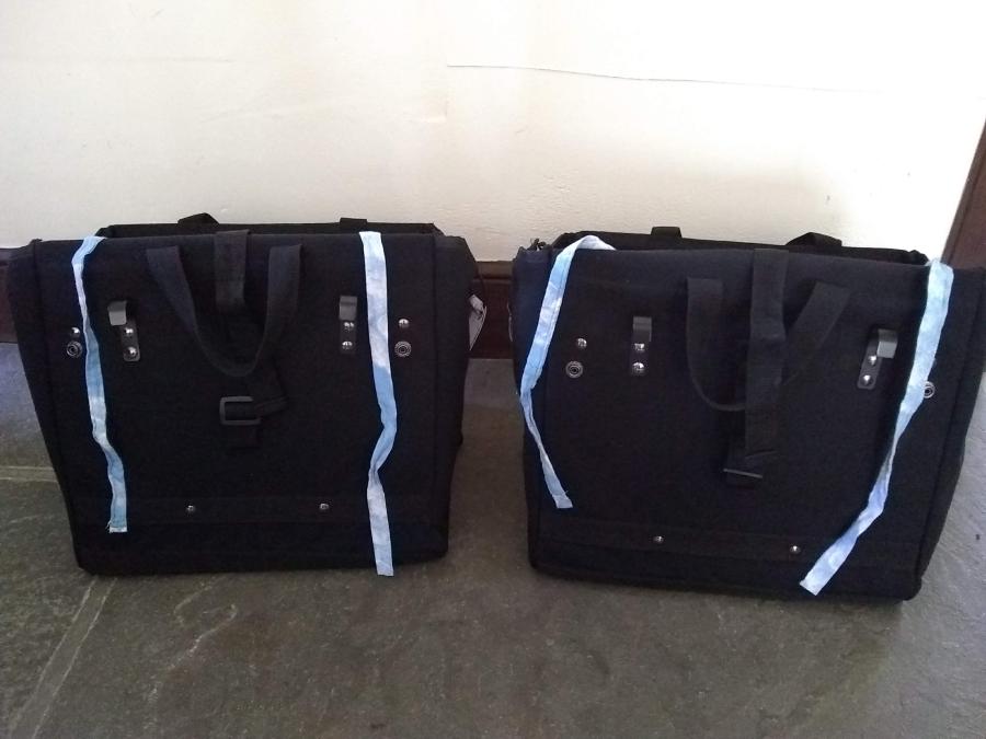black bike panniers, on floor, shown from back side (hooks visible) with added blue cloth ties