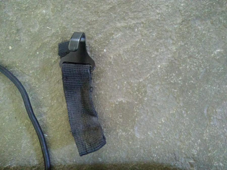 black metal hook on stone floor, attached to grimy and somewhat beat up black cloth loop
