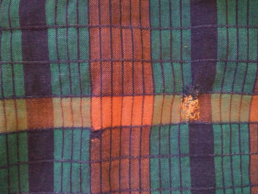 closeup of plaidish fabric, showing one yellow/navy darn on the right and on the left, a small hole in the orange part of the fabric
