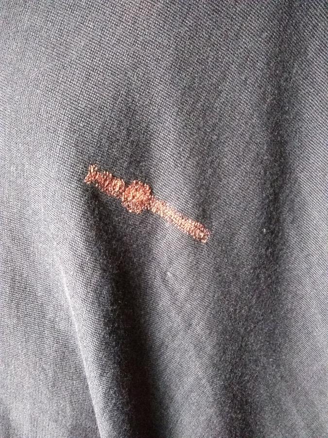 olive brown knit fabric with persimmon colored darn. Darn is shaped kind of like a cross.