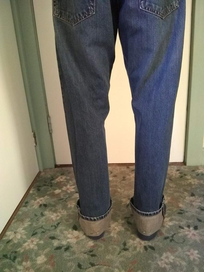 back view of man's legs in blue jeans that are too long (cuffs folded up 3 inches or so)