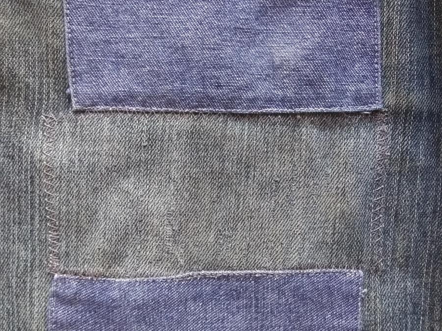 closeup of leg of jeans, with two external patches in contrasting denim bracketing a less visible internal patch (only the zig-zag stitched outlines of the internal patch are visible on the right side.)