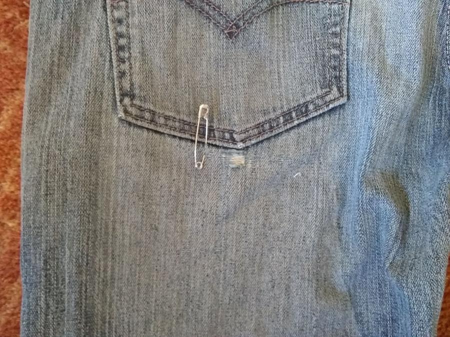 Back of jeans below pocket, with safety pin near frayed fabric right below pocket