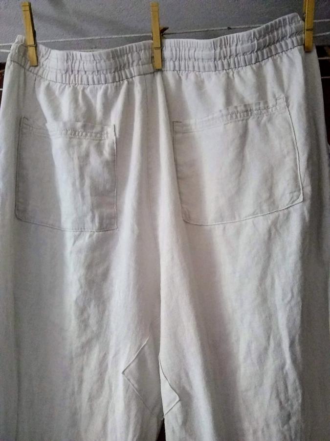 off white linen pants, viewed from backside, hanging on clothesline. Back pockets and barely visible (matching fabric) patch at the seat/crotch.