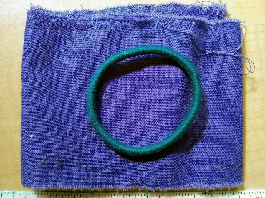 Purple strip of fabric, folded, with blue hair tie elastic on top