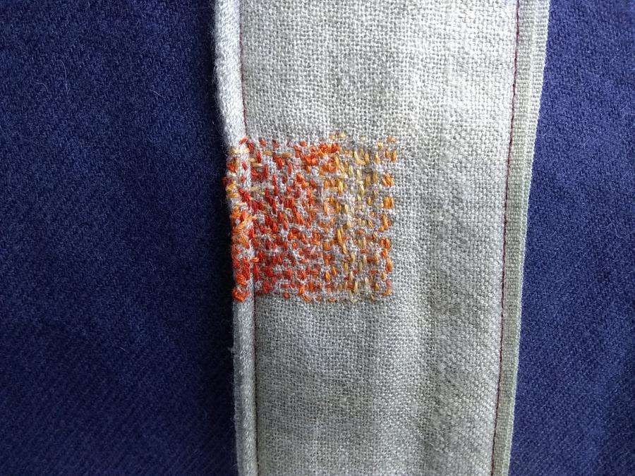 closeup of variegated orange darning on a gray patch over a navy blue blanket