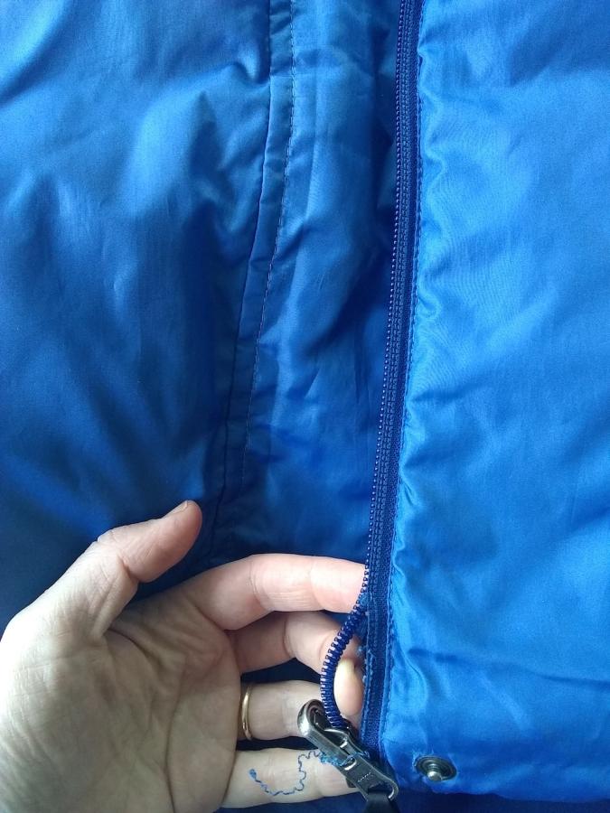 Hand showing that zipper teeth are coming out of zipper of blue down vest