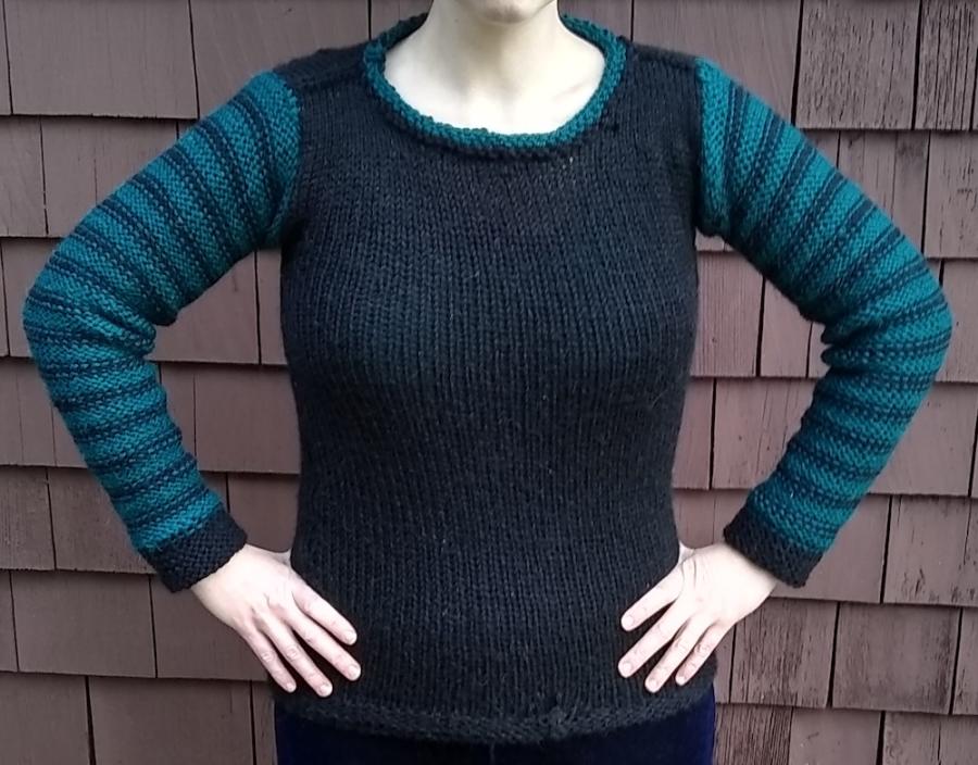 Woman wearing a sweater with black front and green and black striped sleeves (only torso and arms are visible, both hands on hips)