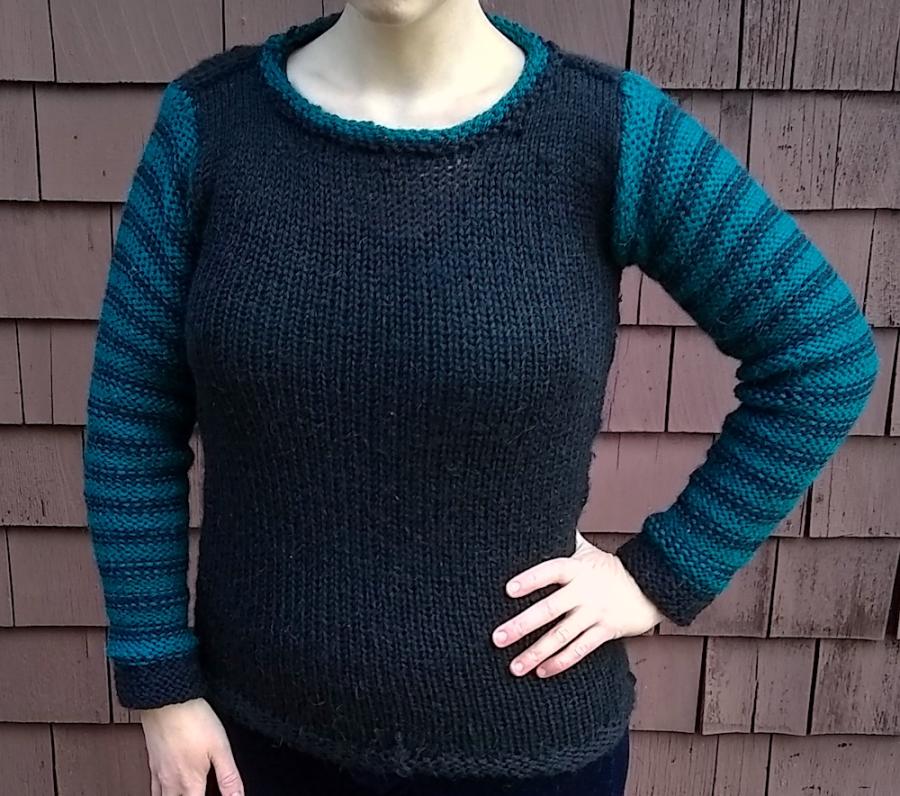 woman's torso, one hand is one her hip, and she's wearing a black sweater with black and green striped sleeves and green trim around the neck